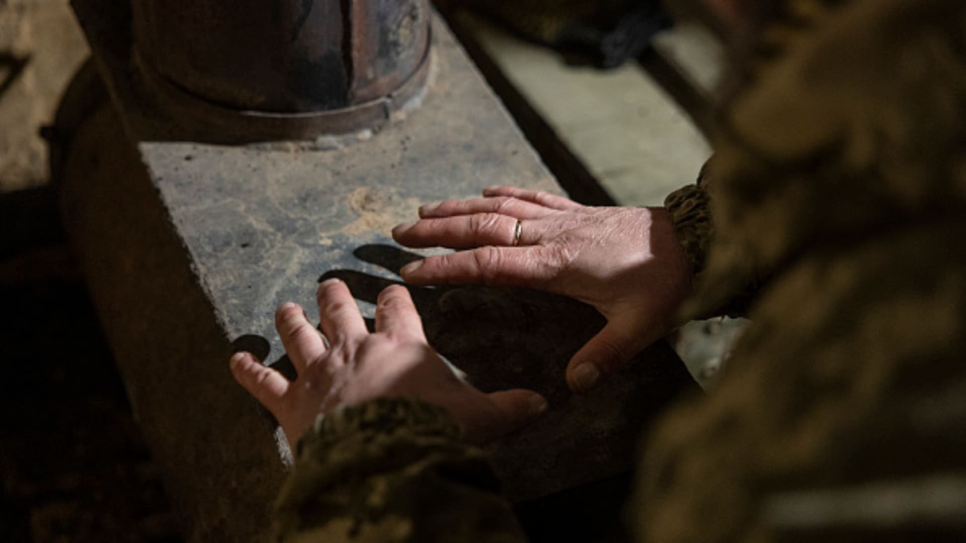 A Ukrainian Marine warms his hands over a wood burning heater inside a bunker at his unit's tank position on February 15, 2023 in the Donbass region of eastern Ukraine. 