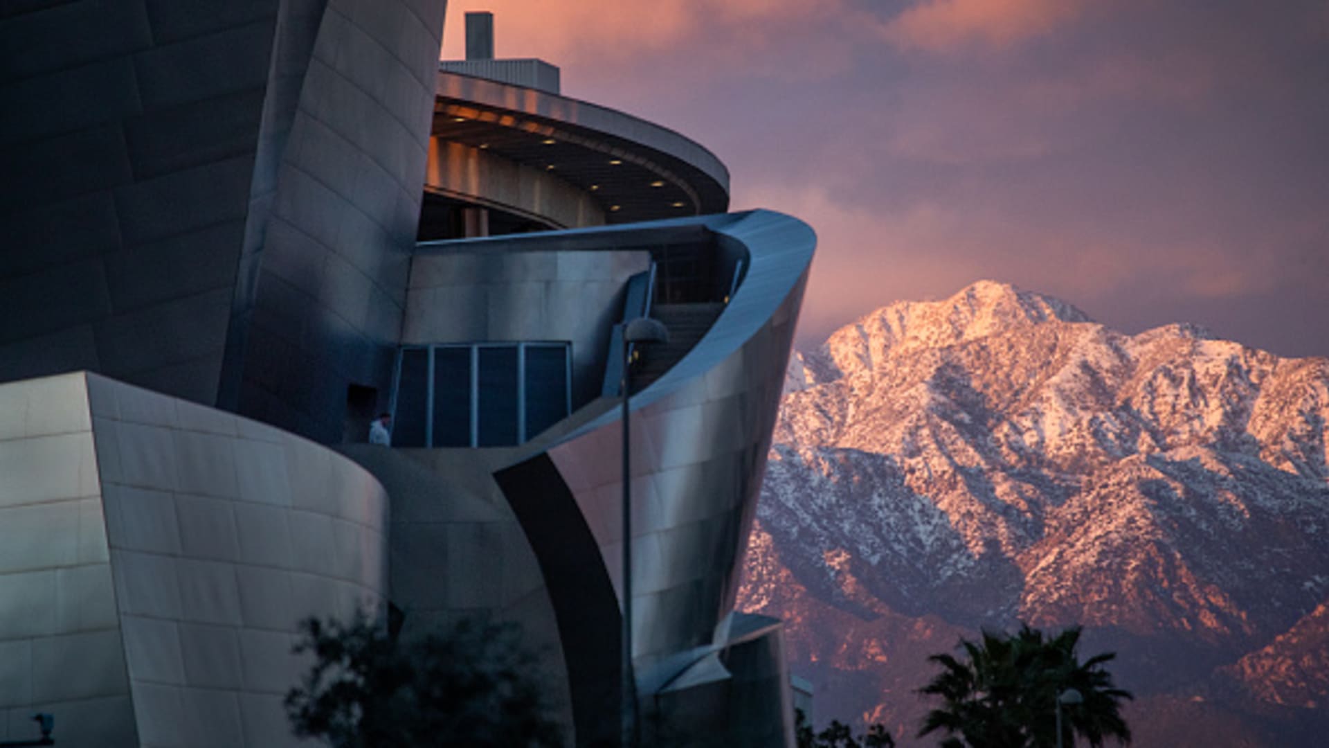 A person gets a high-angle view from the Walt Disney Concert Hall as it is viewed with the snow-capped San Gabriel mountains at sunset after historic rain and snow dumped on Southern California Wednesday, March 1, 2023 in Los Angeles.
