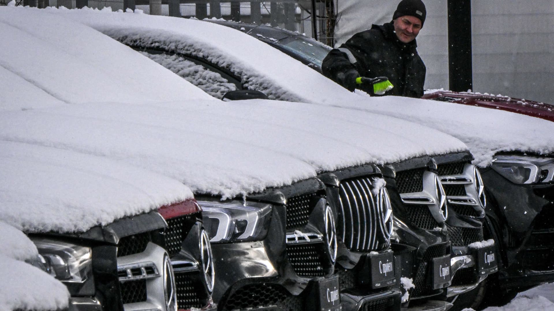 An employee cleans snow from Mercedes-Benz cars parked in front of a Mercedes-Benz dealership in Moscow on February 14, 2023.