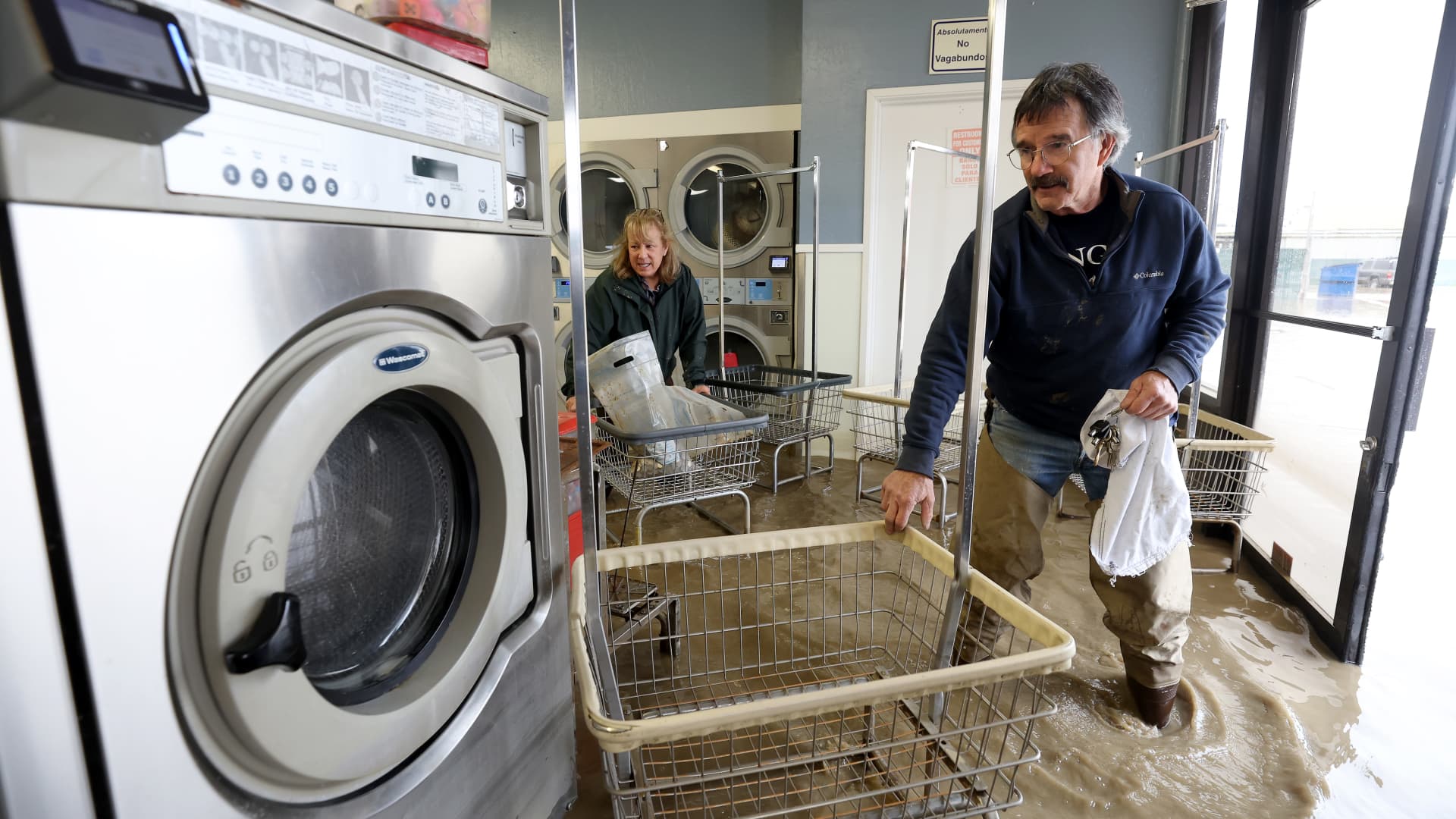 Patrick Cerruti (R) and his wife Pamela Cerruti take coins out of washing machines inside the flooded Pajaro Coin Laundry on March 14, 2023 in Pajaro, California.