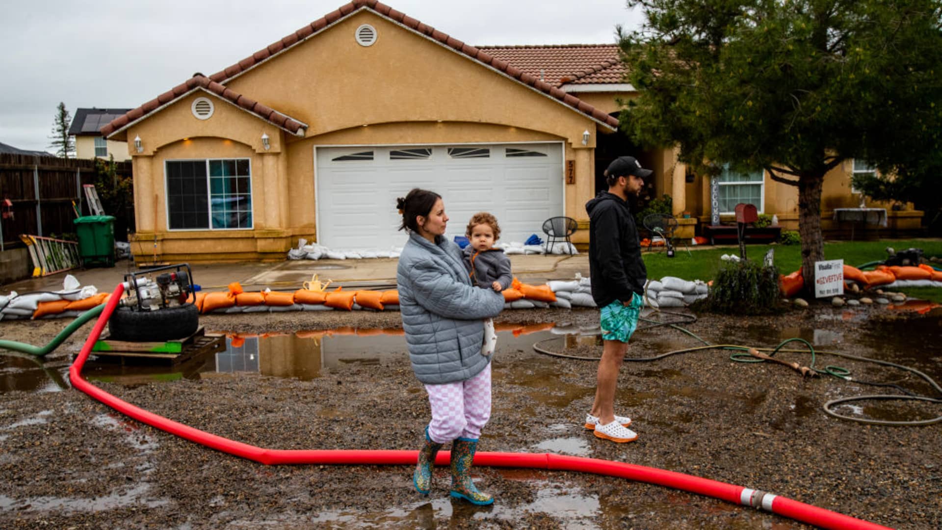 Madisyn Liles holding Luka,1, watches with her husband Keylan as two pumps continue to work throughout the day to remove flood water from their home after Tuesday nights heavy rains on March 15, 2023 in Woodlake, California.