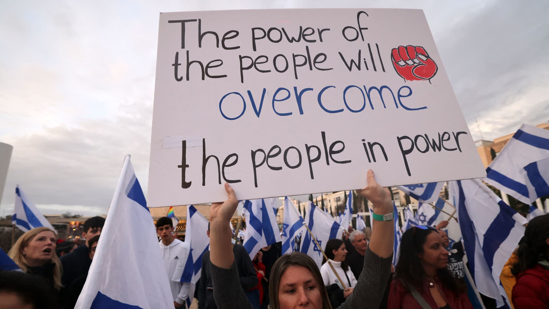 Demonstrators wave national flags and raise placards during a rally against the Israeli government's controversial judicial overhaul bill in Tel Aviv, on March 25, 2023.