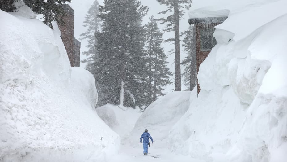 МАММОТ-ЛЕЙКС, КАЛИФОРНИЯ - 28 МАРТА: Человек прогуливается возле сугробов, скрывающих кондоминиумы, когда в горах Сьерра-Невада выпадает снег из еще одной штормовой системы, которая, по прогнозам, принесет сильный снег на более высокие высоты 28 марта 2023 года в Маммот-Лейкс, Калифорния. Тихоокеанский шторм приносит широко распространенные дожди и горный снег на западное побережье США в Северной Калифорнии и Орегоне. После нескольких лет засухи средний уровень снежного покрова в штате Калифорния может побить рекорд за несколько лет.