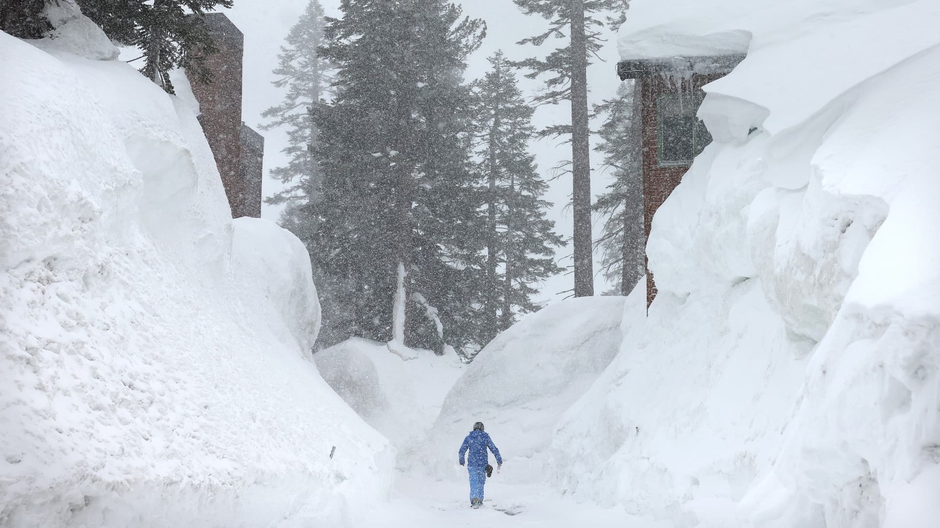 A person walks near snowbanks obscuring condominiums as snow falls in the Sierra Nevada mountains from yet another storm system which is predicted to bring heavy snow to higher elevations on March 28, 2023 in Mammoth Lakes, California.