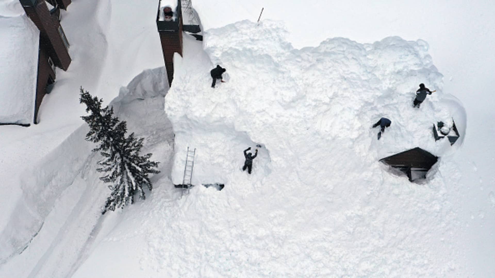 In an aerial view, workers remove snow from the roof of a condominium complex in the Sierra Nevada mountains, amid snow piled up from new and past storms, after yet another storm system brought heavy snowfall further raising the snowpack on March 29, 2023 in Mammoth Lakes, California. 
