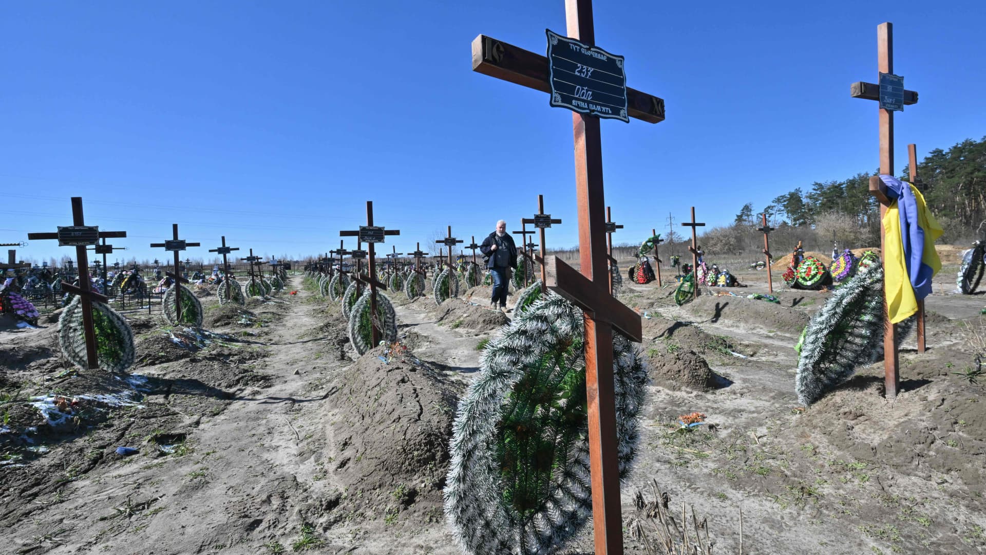 A man walks among graves of unidentified local people who were killled in the Ukrainian town of Bucha, northwest of Kyiv on March 30, 2023, a day before the celebration of the first anniversary of the Bucha liberation from Russian troops on March 31.