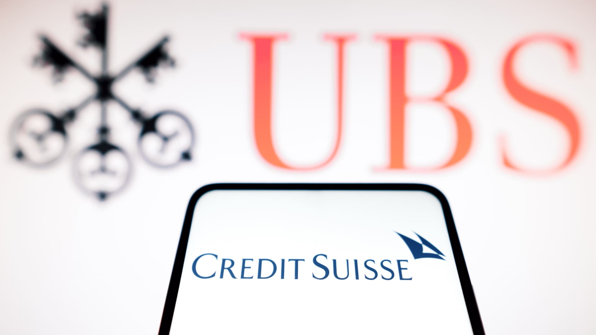 The Credit Suisse logo seen displayed on a smartphone and UBS logo on the background.