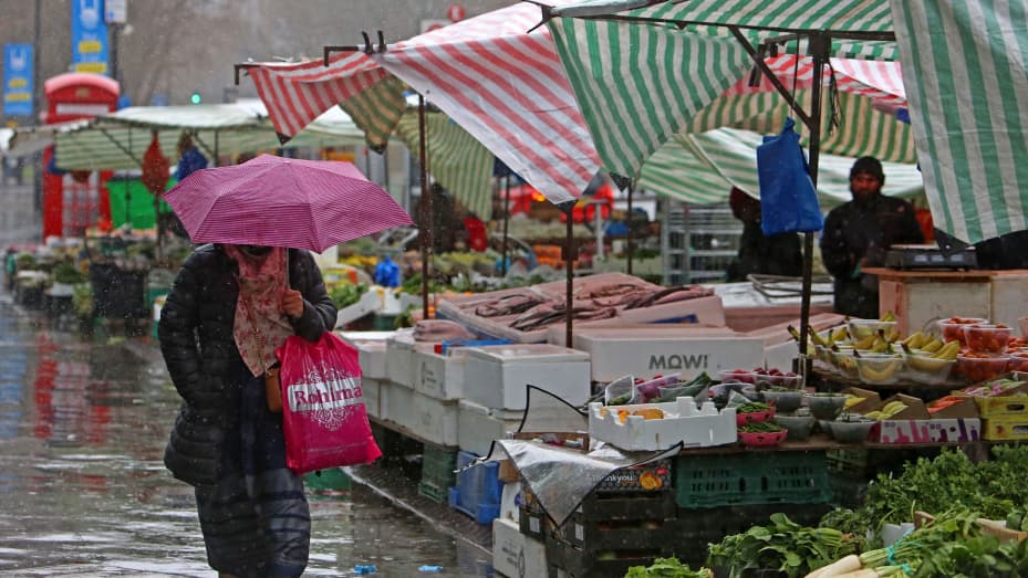 LONDRES - 31 de marzo de 2023: Un peatón se protege de la lluvia mientras pasa junto a frutas y verduras expuestas a la venta en un mercado en el este de Londres.  Los nuevos datos publicados el miércoles 19 de abril revelaron que los precios de los alimentos y las bebidas no alcohólicas aumentaron un 19,2 % en el año hasta marzo de 2023, el aumento anual más pronunciado en más de 45 años.