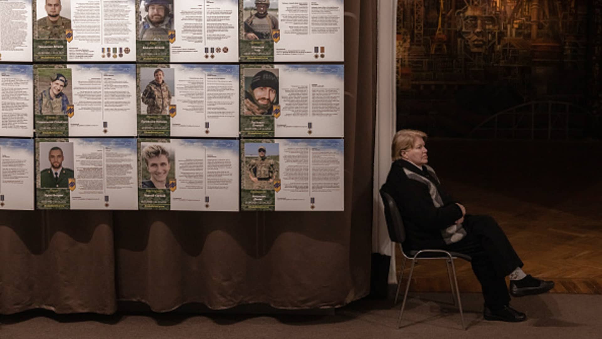 A museum worker sits next to the portraits of members of the 'Azov' unit that were killed last year in Mariupol during the Russian attack, at the part of the exhibition dedicated to defending of Mariupol's Azovstal on April 26, 2023 at the National Museum of the History of Ukraine in Kyiv, Ukraine.