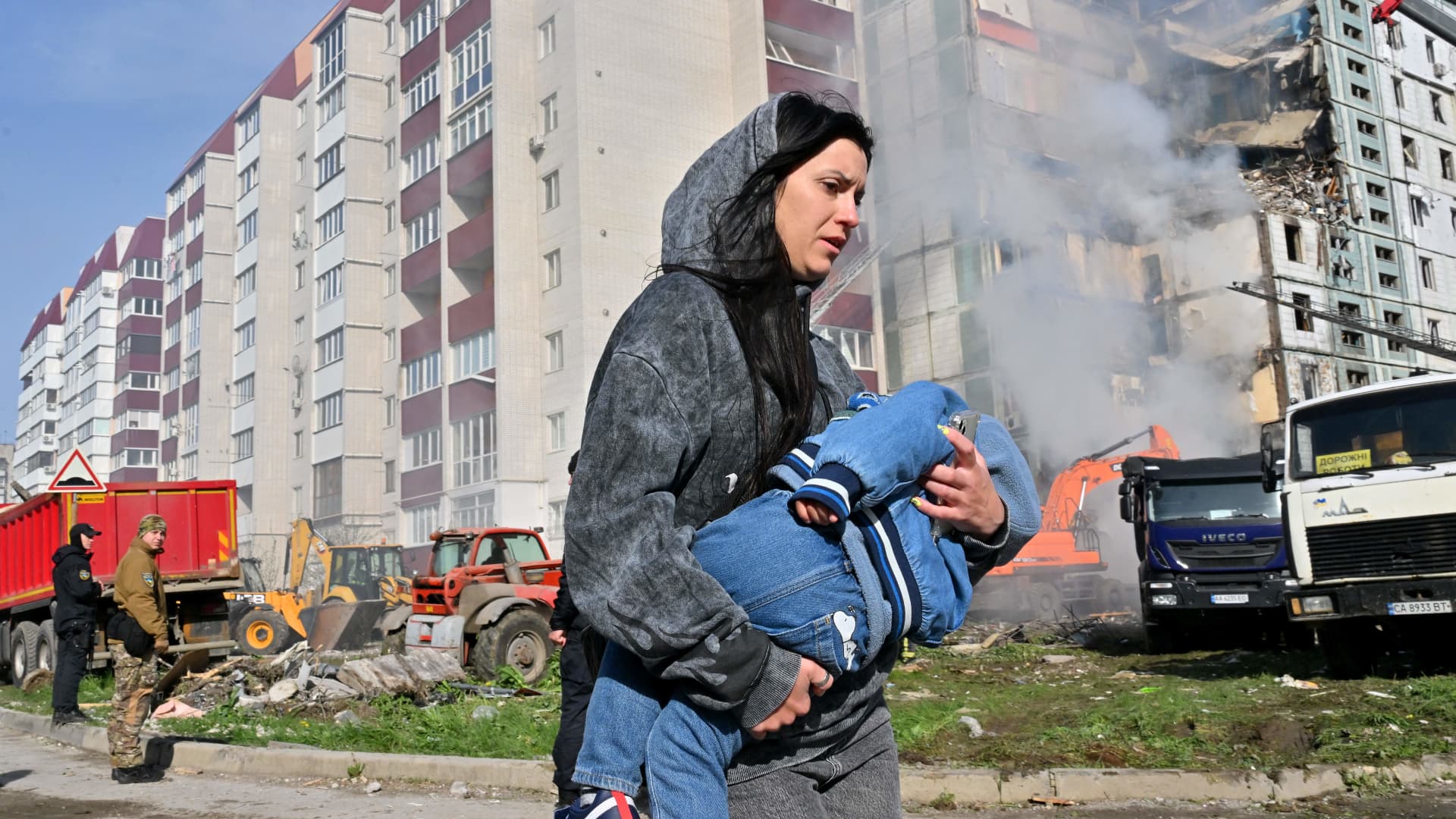 A woman walks past damaged residential buildings as she carries a child in Uman, around 215km southern Kyiv, on April 28, 2023, after Russian missile strikes targeted several Ukrainian cities overnight.