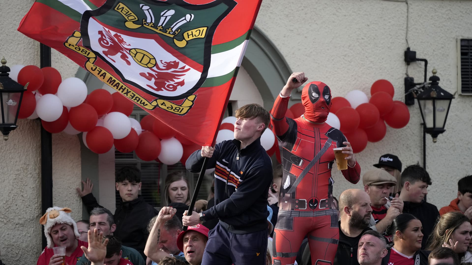 WREXHAM, Wales - May 2, 2023: Wrexham AFC fans celebrate during a bus parade following their league title win. One fan has donned the costume of Deadpool, the comic book character played by co-owner Ryan Reynolds.