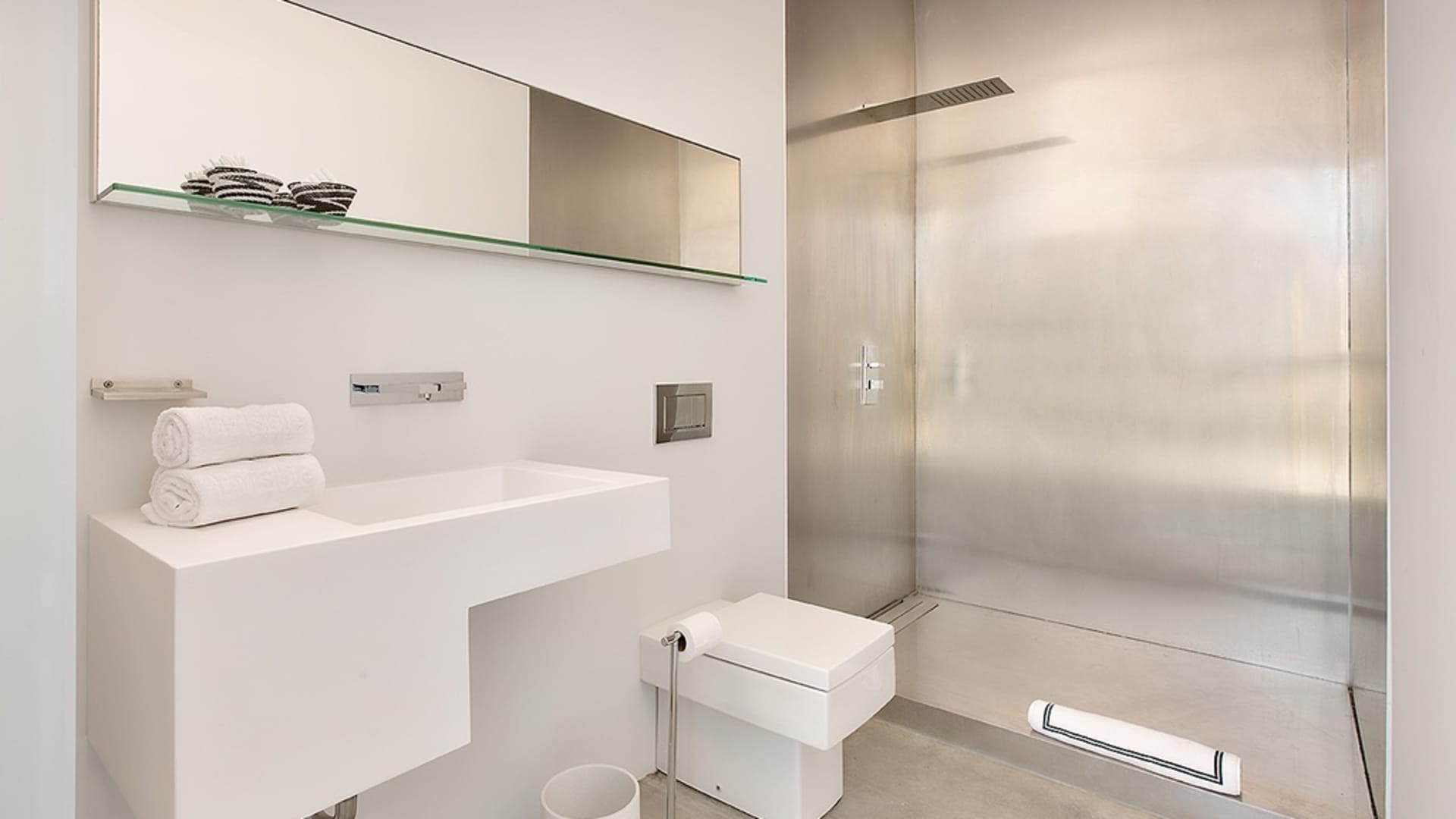The guest bedroom's minimalist ensuite bath includes cement floors and a stainless steel shower.
