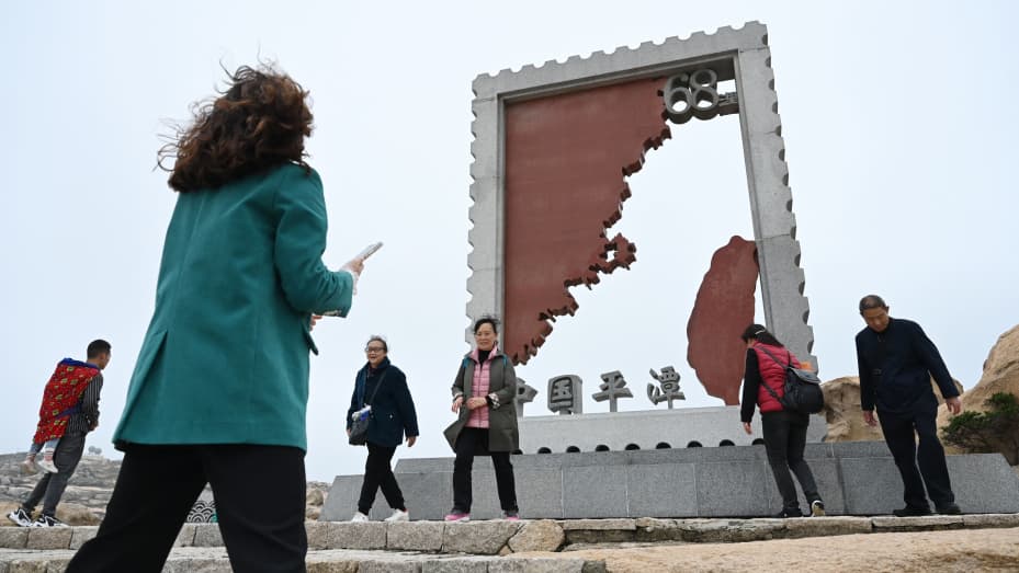 Chinese tourists walk past an installation depicting Taiwan (R) and mainland China at a tourist area on Pingtan island, the closest point to Taiwan, in China's southeast Fujian province on April 6, 2023.