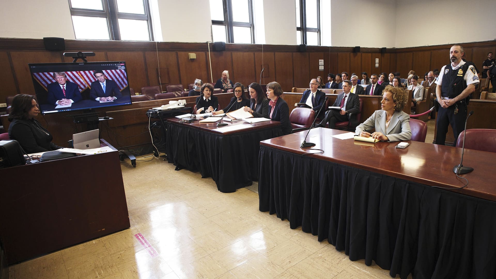 Former president Donald Trump, left on screen, and his attorney, Todd Blanche, right on screen, appear by video, as his other attorney Susan Necheles, right, looks on, before a hearing begins in Manhattan criminal court, in New York, Tuesday, May 23, 2023. Trump made a video appearance Tuesday in his New York criminal case, with the judge tentatively setting a trial date for late March of next year.