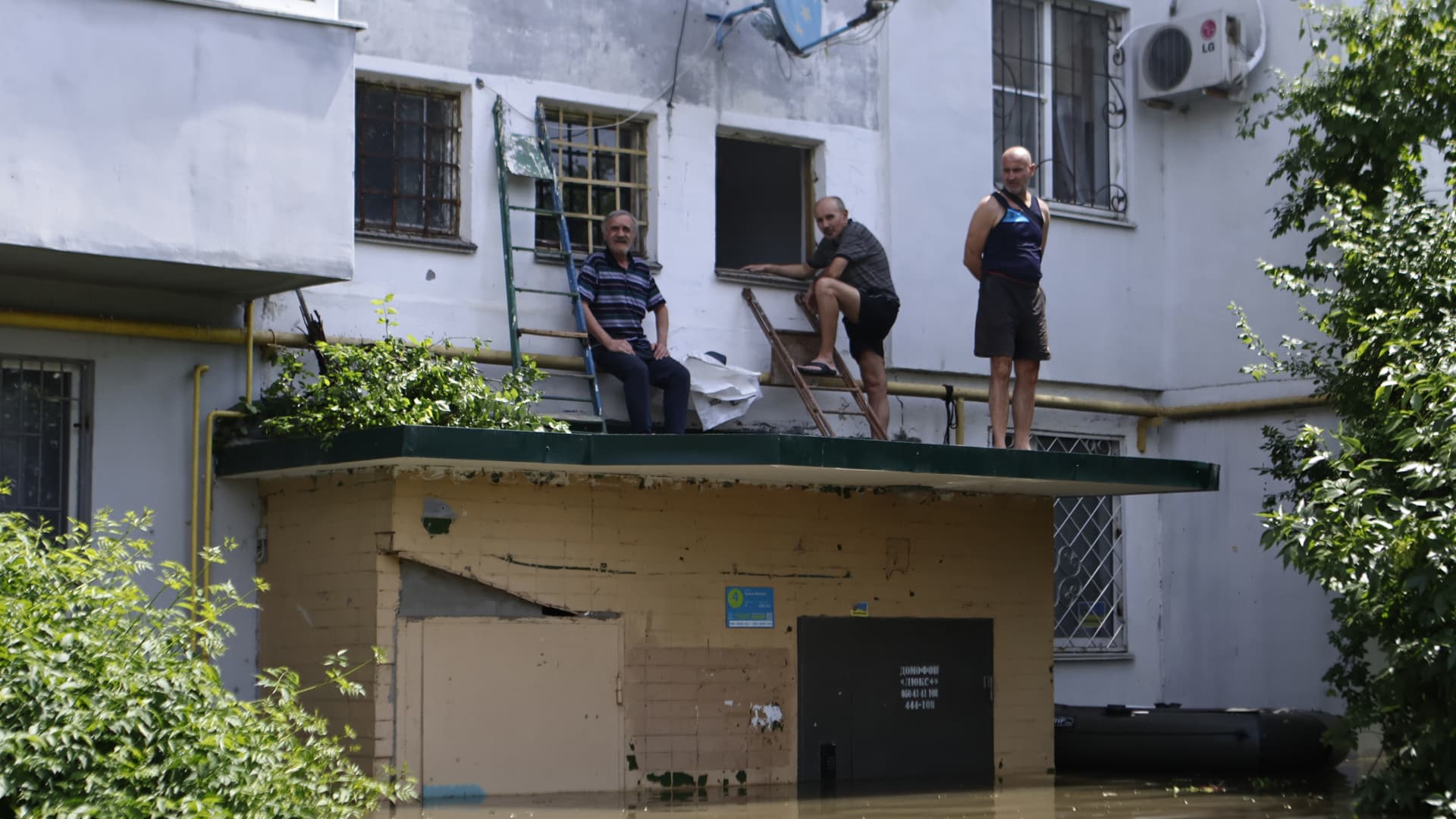 Local residents stand on the roof of the entrance to a residential building in the flooded area of the city on June 7, 2023 in Kherson, Ukraine.