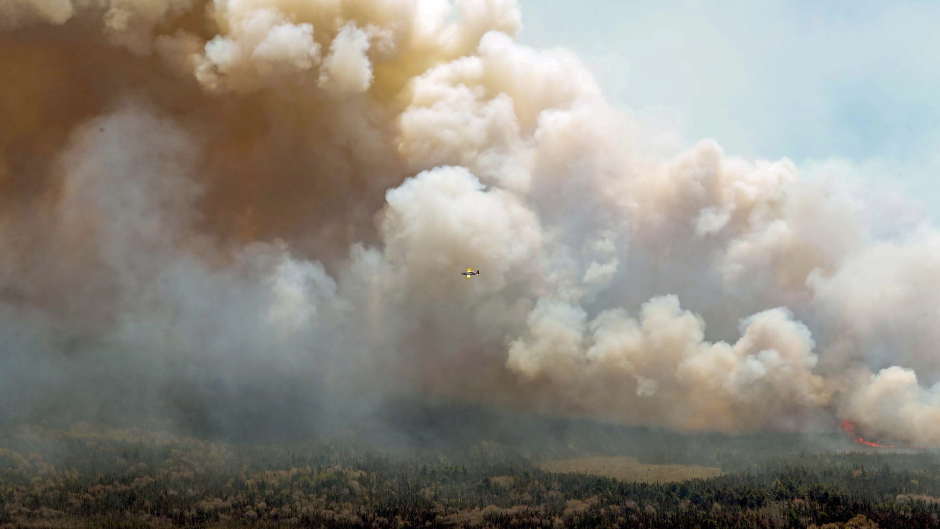 In this aerial image, an aircraft, center, flies near a wildfire burning near Barrington Lake in Shelburne County, Nova Scotia, on Wednesday, May 31, 2023.