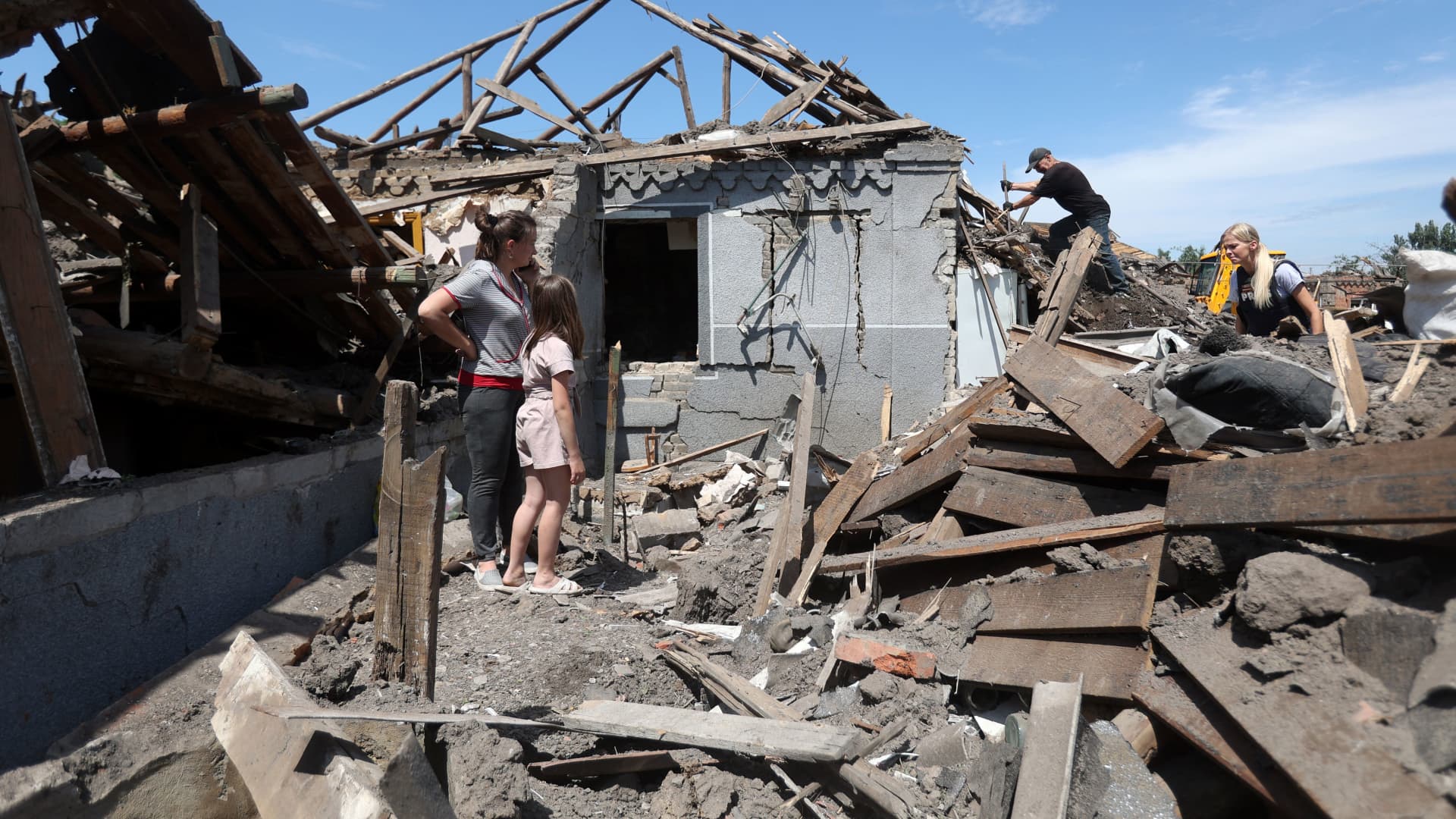 Iedzīvotāji stāv starp savu māju drupām, kad pašvaldības darbinieki tīra gruvešus pēc Krievijas uzbrukuma Kramatorskai 2023. gada 14. jūnijā.