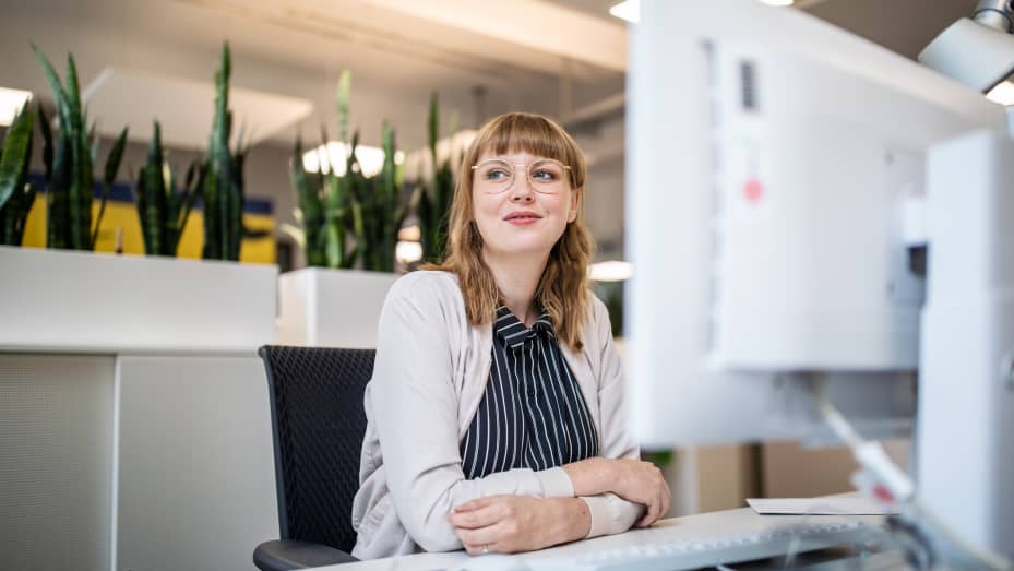 Thoughtful businesswoman looking away while sitting at desk in creative office