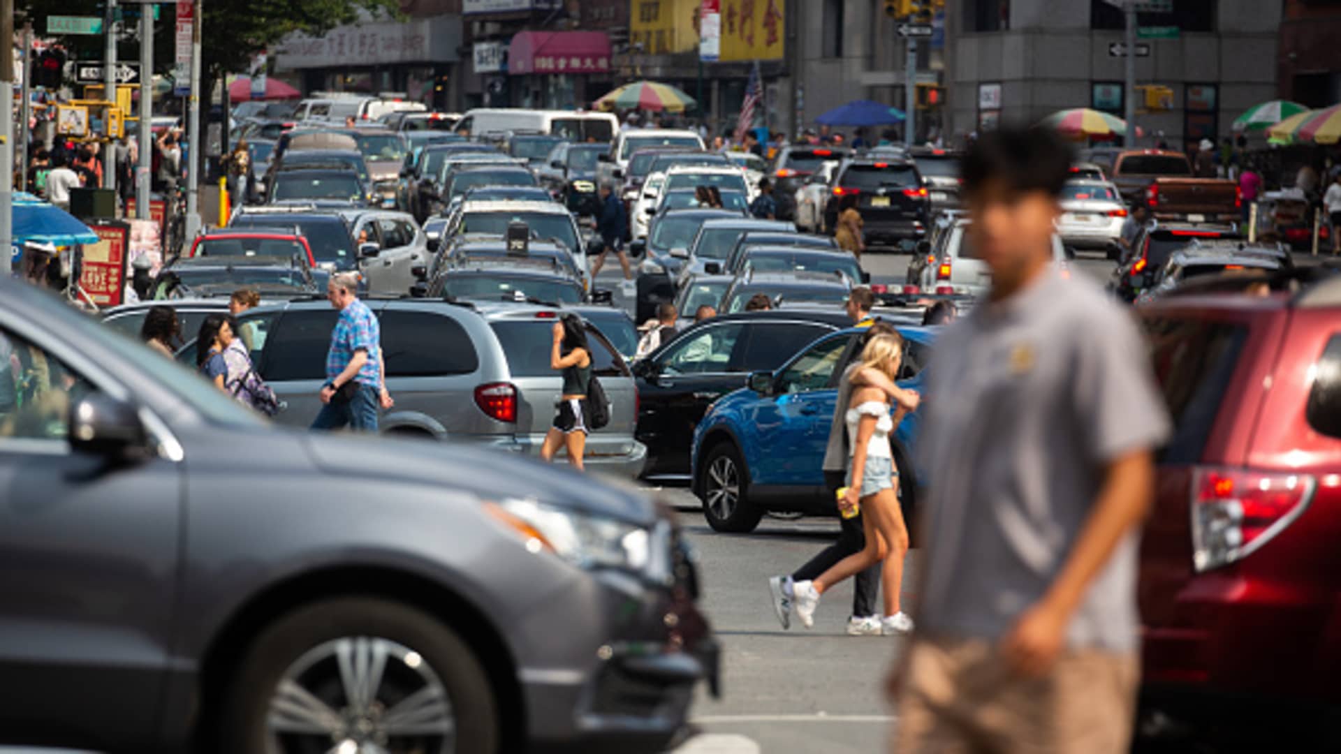 Pedestrians cross a street past traffic in the Midtown neighborhood of New York, June 17, 2023.