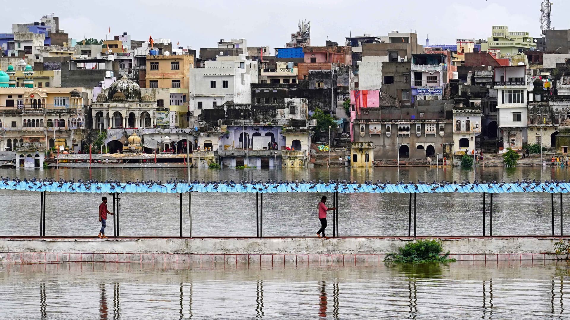 People walk amid the swollen lake after heavy monsoon rains in Pushkar, in India's Rajasthan state on July 10, 2023.