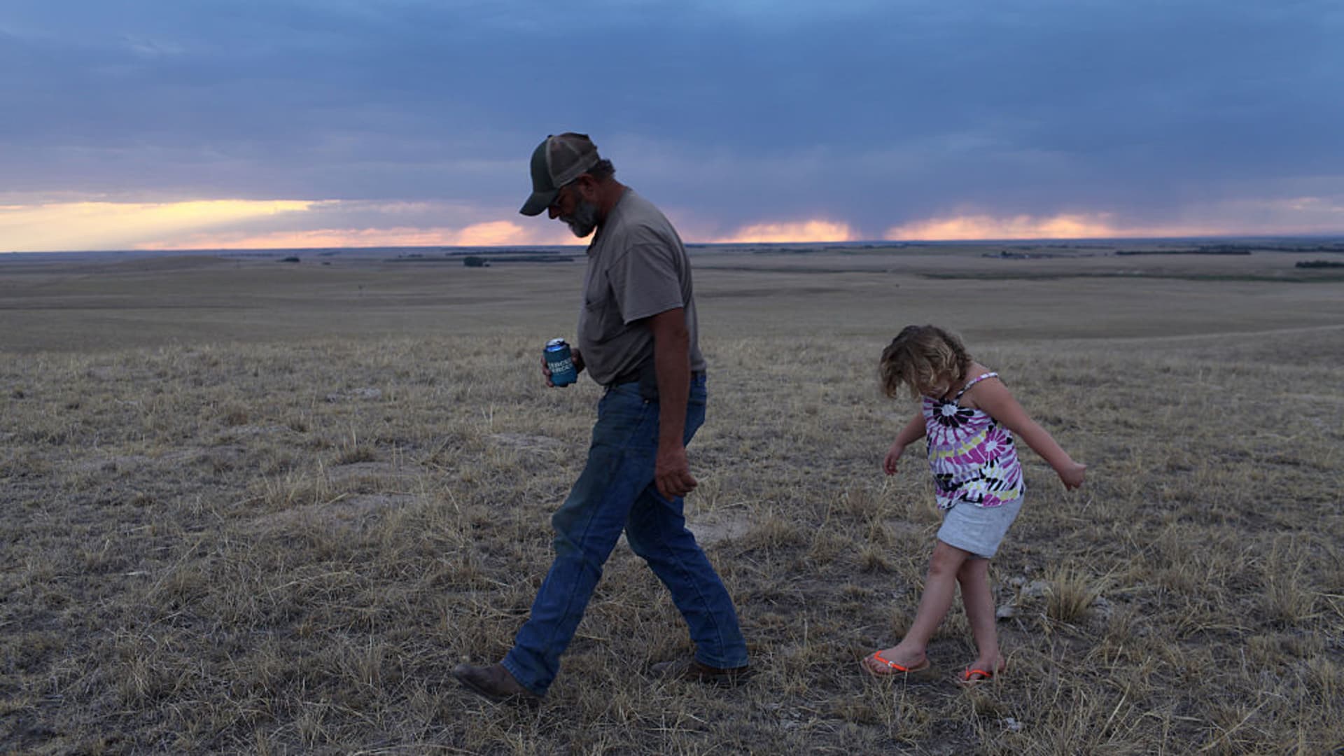 On an evening stroll, Jim Mracek leads his grandaughter across the drought stricken fields of the cattle ranch that he looks after, keeping an eye out for burrs because she is wearing sandals.