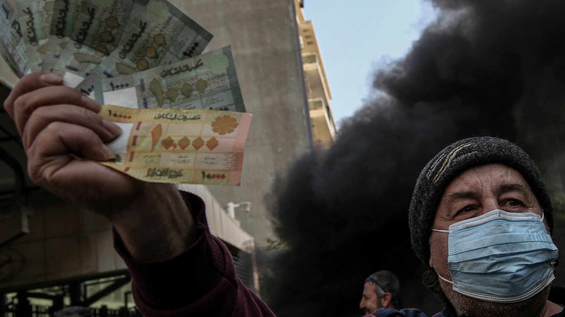 An anti-government Lebanese activist displays Lebanese bills during a protest outside the country's central bank against the continuing downward spiral of the Lebanese pound against the dollar and Riad Salameh's arrest, under investigation by five European countries.