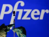 Una imagen ilustrativa de una persona que sostiene una jeringa médica y un vial de vacuna frente al logotipo de Pfizer que se muestra en una pantalla.