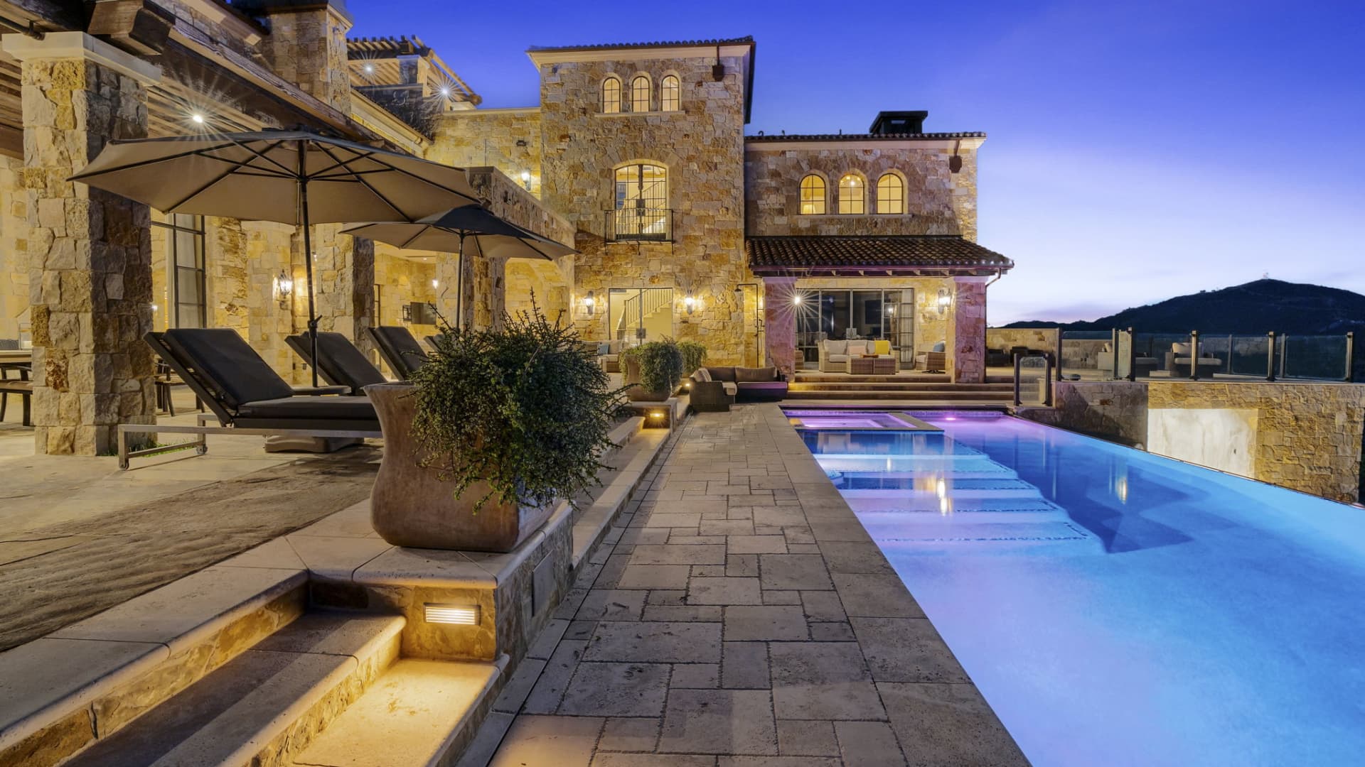 The home's tiered stone deck and infinity pool at sunset.