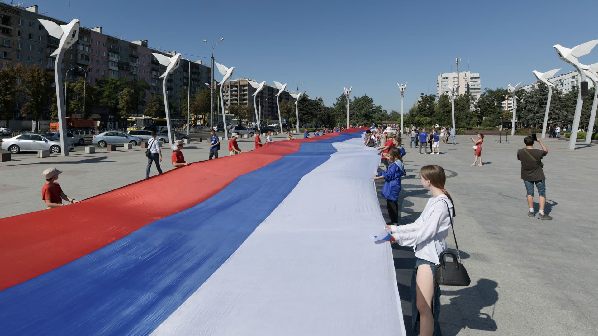 Local residents, activists and members of administration hold a 100-meter Russian flag during Russia's National Flag Day celebrations in the central square of Mariupol, southern Ukraine, on August 22, 2023.