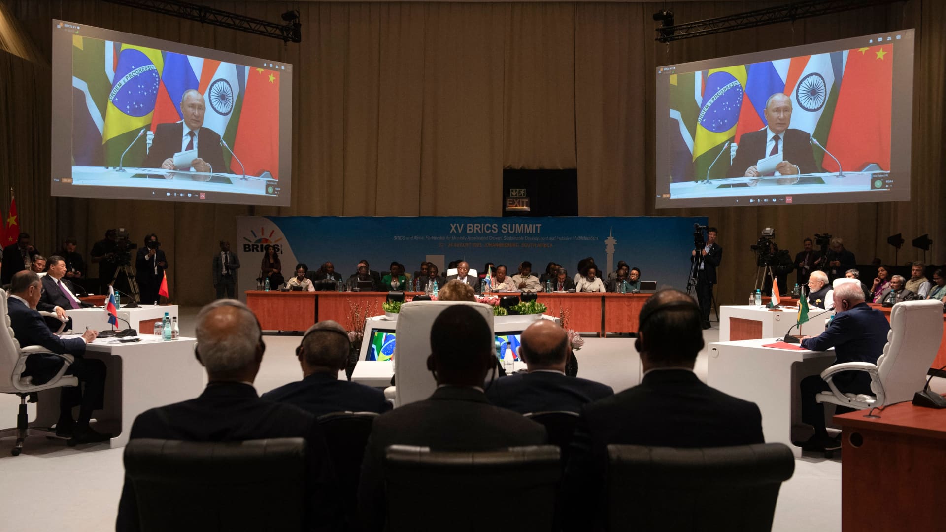 Delegates listen on during the plenary session as Russian President Vladimir Putin delivers his remarks via video-link during the 2023 BRICS Summit at the Sandton Convention Centre in Johannesburg on August 23, 2023.