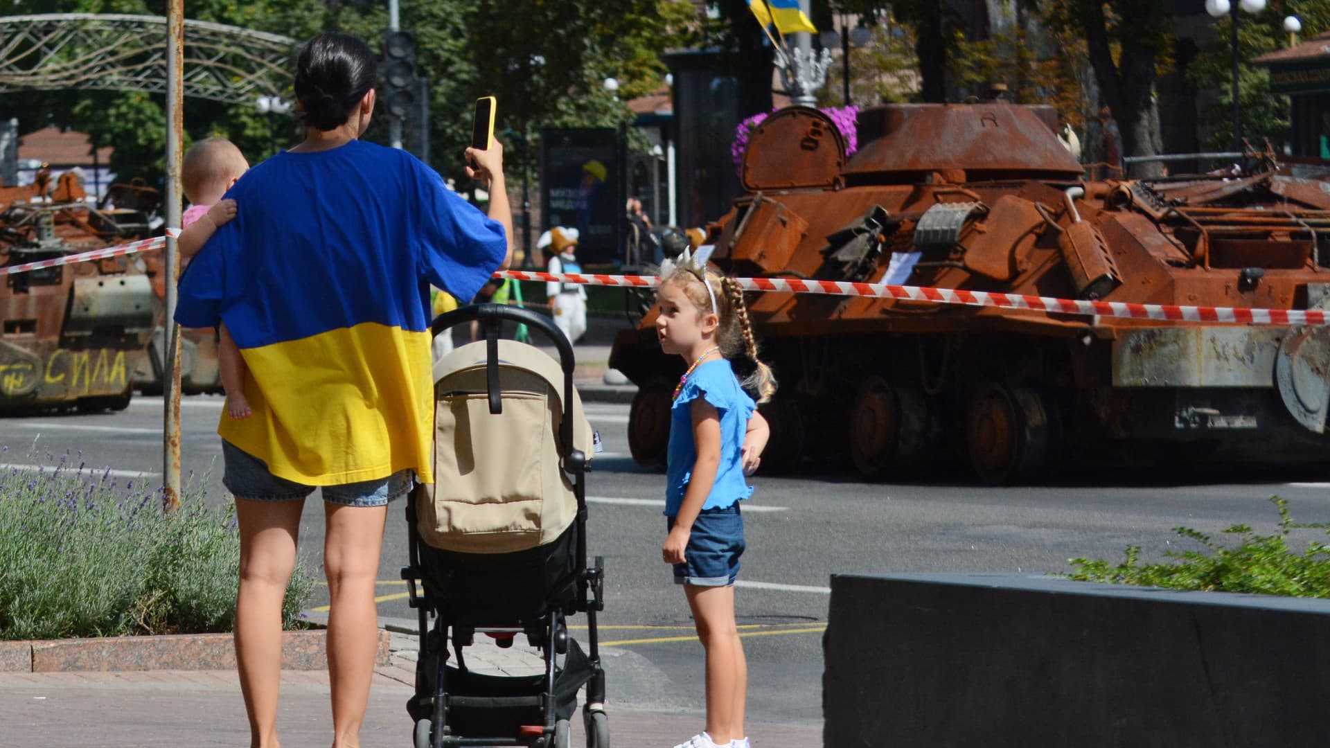 A woman wearing a T-shirt in the colors of the Ukrainian flag, walks with two children and takes photos of destroyed Russian military vehicles displayed on Khreschatyk Street during an exhibition on August 23, 2023 in Kyiv, Ukraine. 