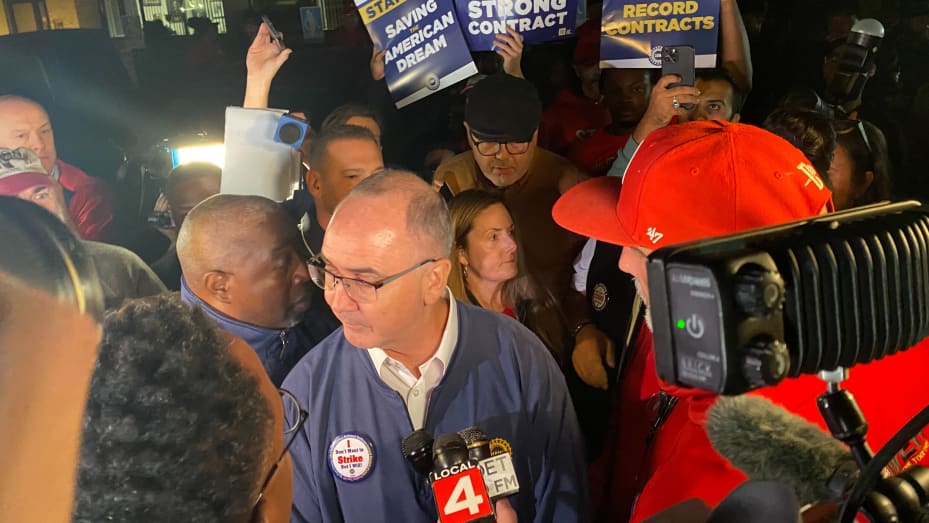 UAW President Shawn Fain, center, talks to reporters as union members strike outside a Ford plant in Wayne, Michigan, Sept. 15, 2023.