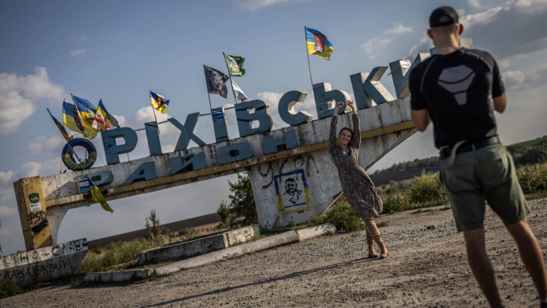 A young woman poses in front of a sign near the frontline town of Orikhiv. The town, which once had almost 14,000 inhabitants, is just a few kilometers from the current front line and almost no one lives there today; most of the houses are either completely destroyed or uninhabitable.