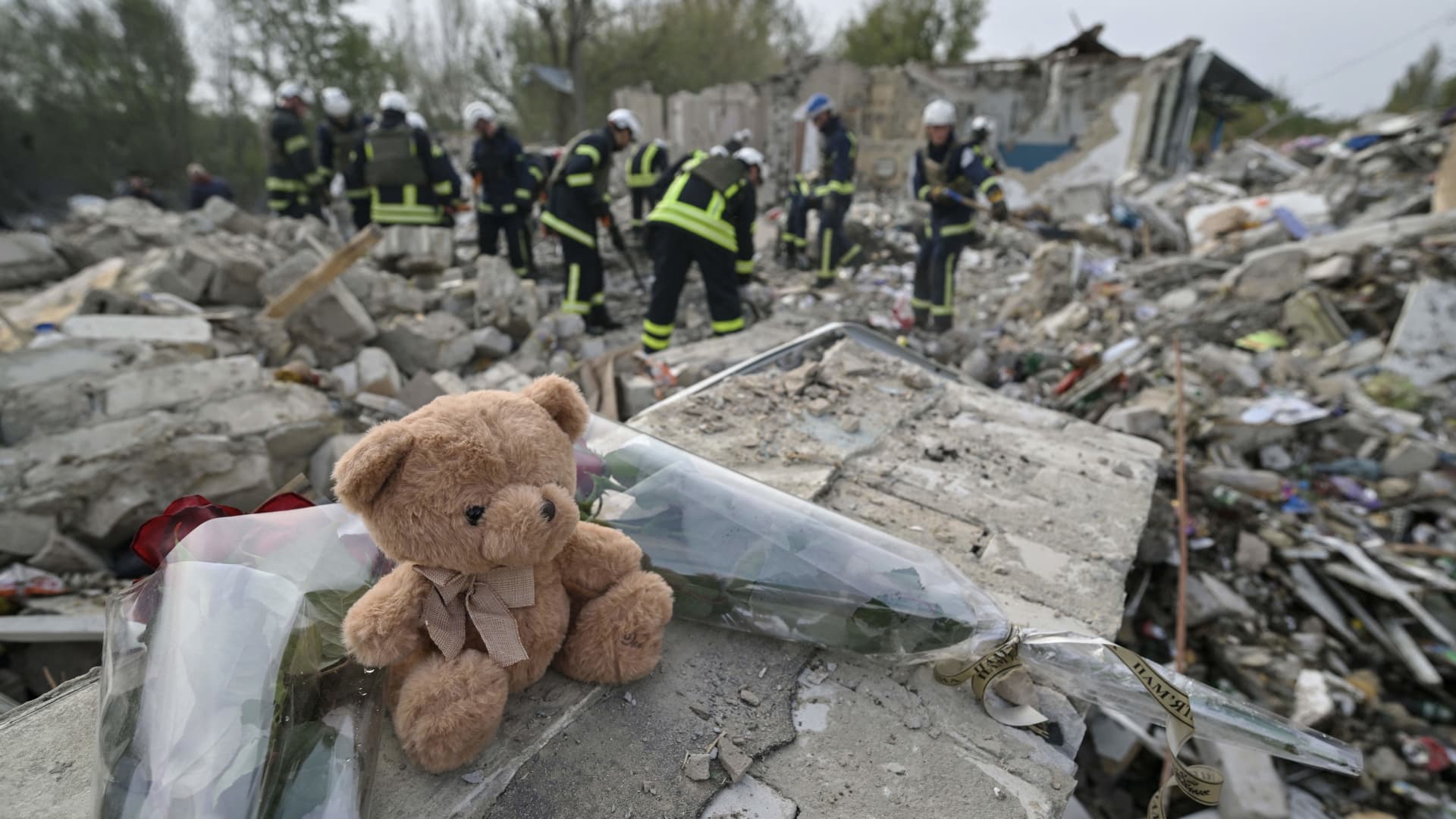 A teddy bear and flowers are displayed on the fragment of a wall as Ukrainian emergency personnel clear debris on the site of a Russian strike which hit a shop and cafe in the village of Groza, some 30 kilometres west of Kupiansk, on October 6, 2023, amid the Russian invasion of Ukraine.