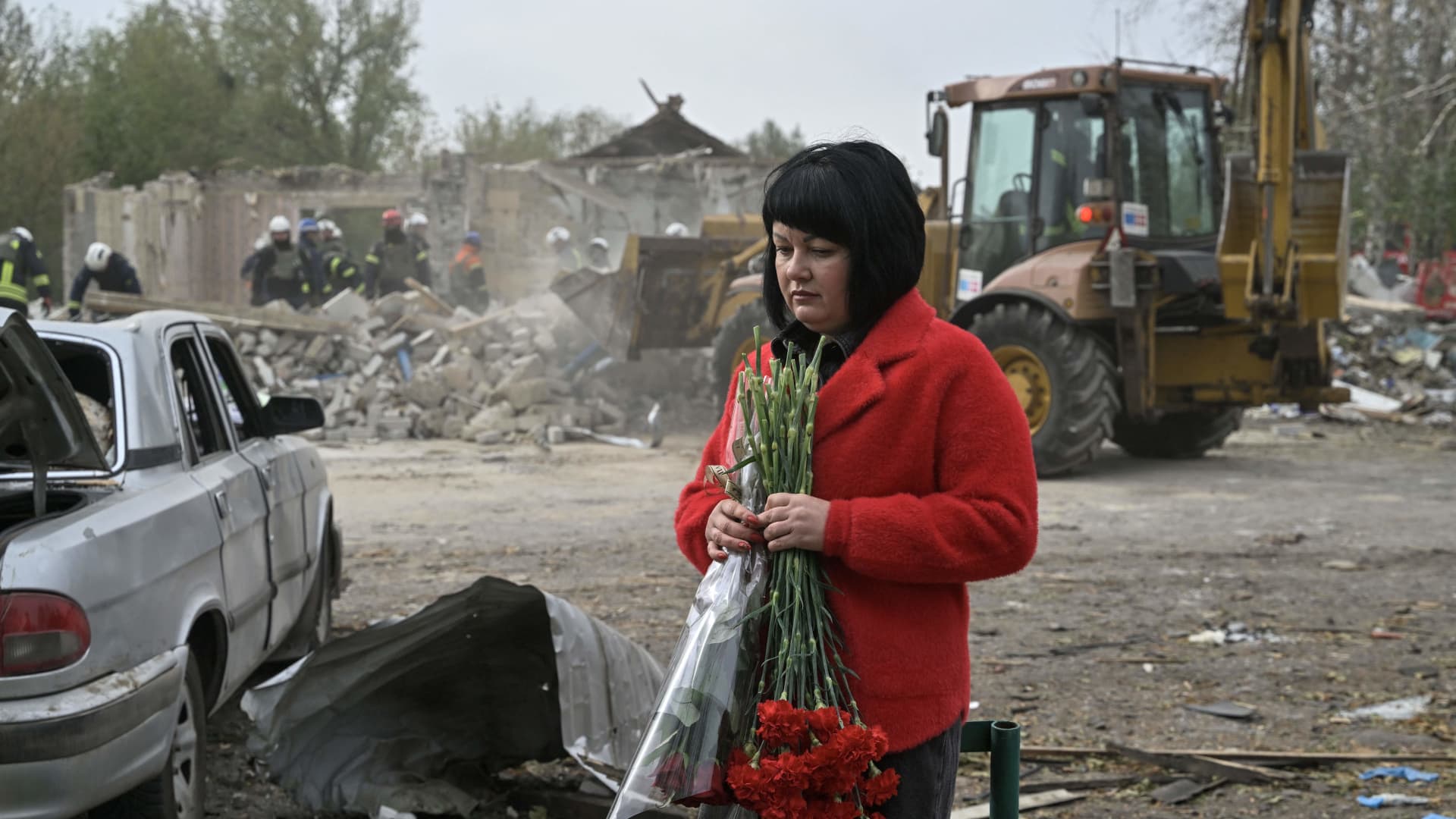 A woman holds flowers as Ukrainian rescuers work to remove debris following a Russian strike which hit a shop and cafe in the village of Groza, some 30 kilometres west of Kupiansk, on October 6, 2023. 