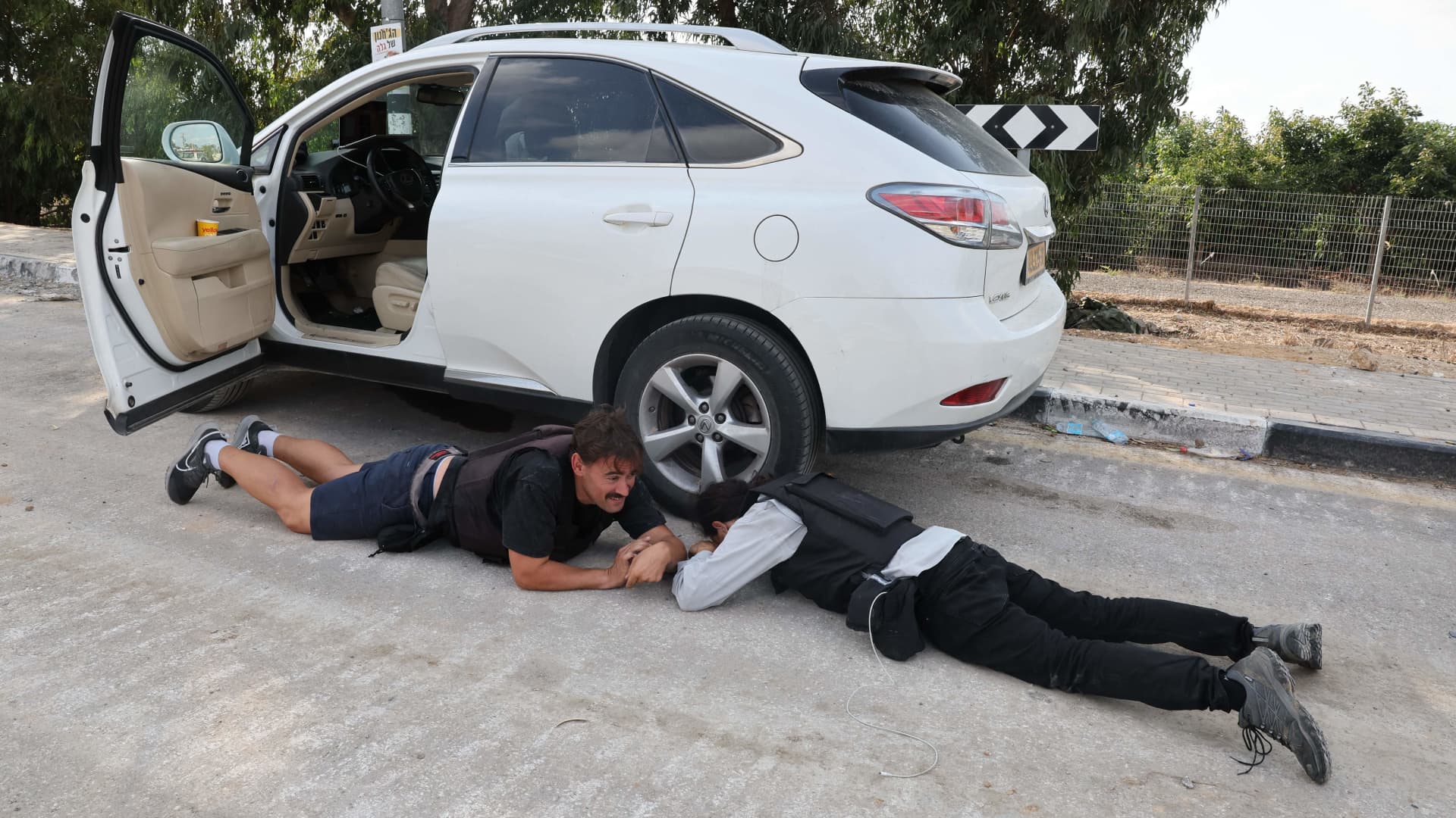 Israeli journalists take cover during a rocket attack from Gaza in the southern Israeli kibbutz of Kfar Aza near the border with the Palestinian territory, on October 10, 2023.