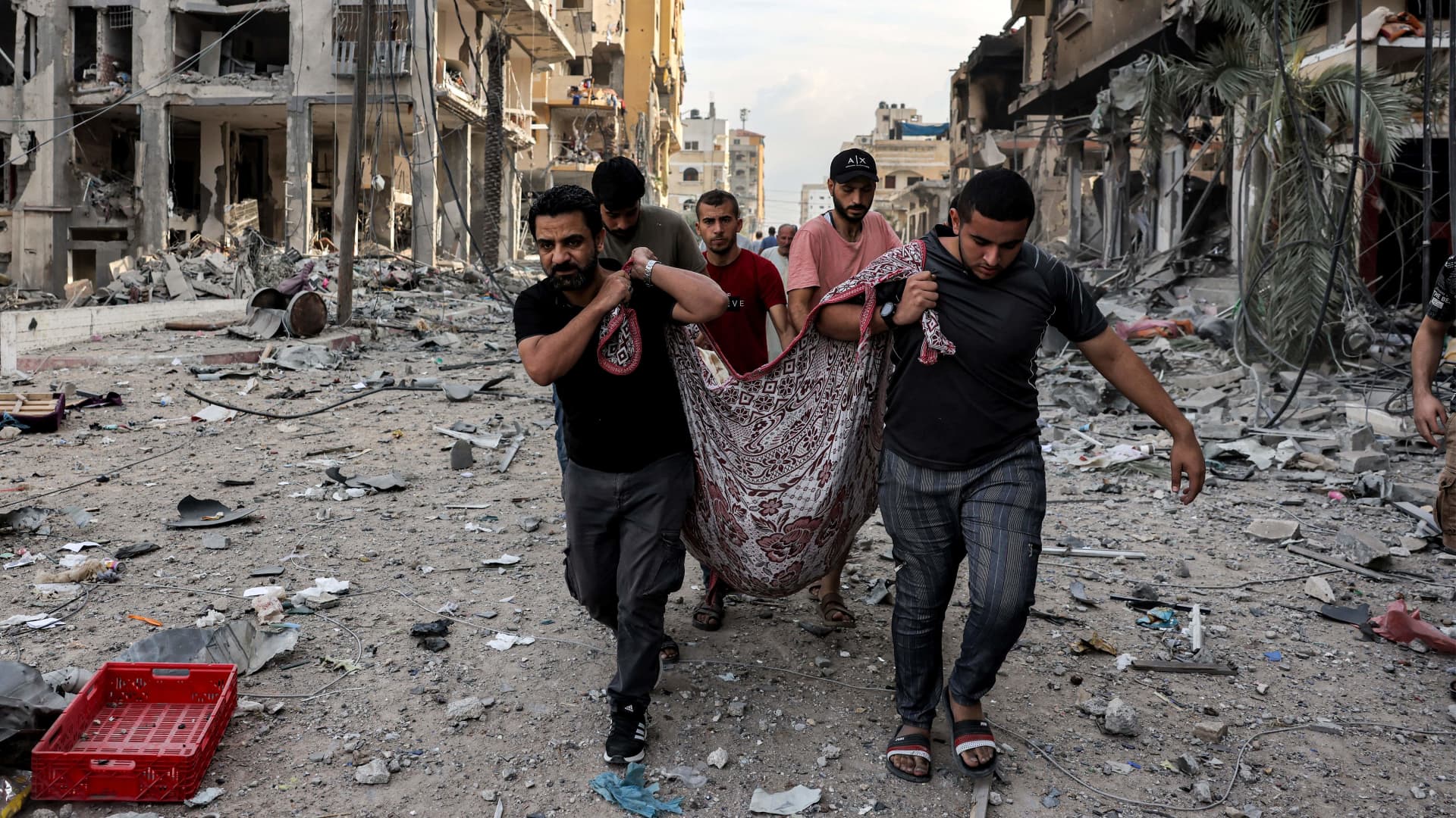 Palestinian men carry away the body of a person killed by Israeli bombardment along a debris-littered street in al-Karama district in Gaza City on Oct. 11, 2023.