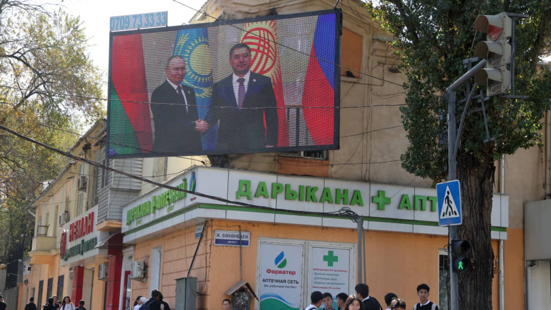 Kyrgyz people walk past to an electronic panel with photo of Russian President Vladimir Putin shaking hands with Kyrgyz President Sadyr Japarov, October 11,2023, in Bishkek, Kyrgyzstan.