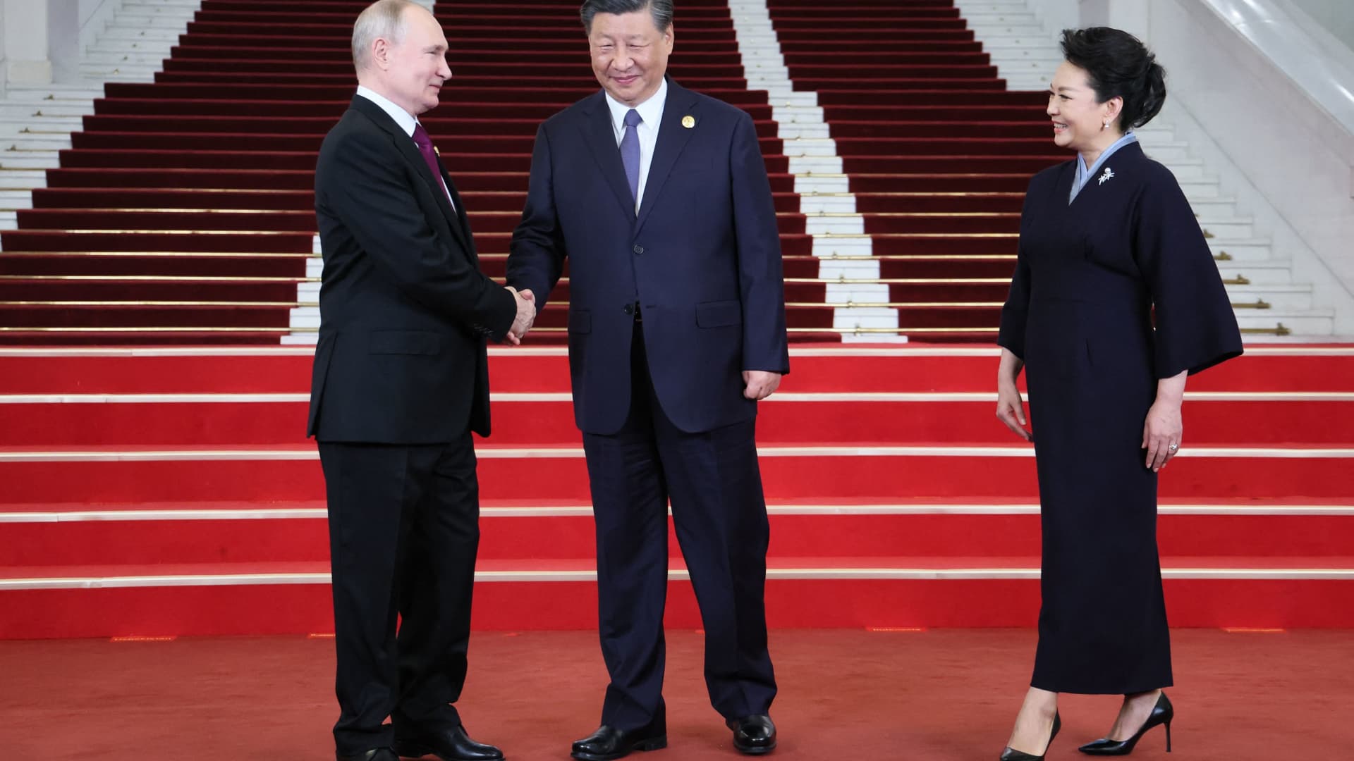 A pool photograph distributed by Russian state owned agency Sputnik shows Russia's President Vladimir Putin and China's President Xi Jinping shaking hands as the wife of the Chinese leader, Peng Liyuan, stands nearby during a welcoming ceremony at the Third Belt and Road Forum in Beijing on October 17, 2023.