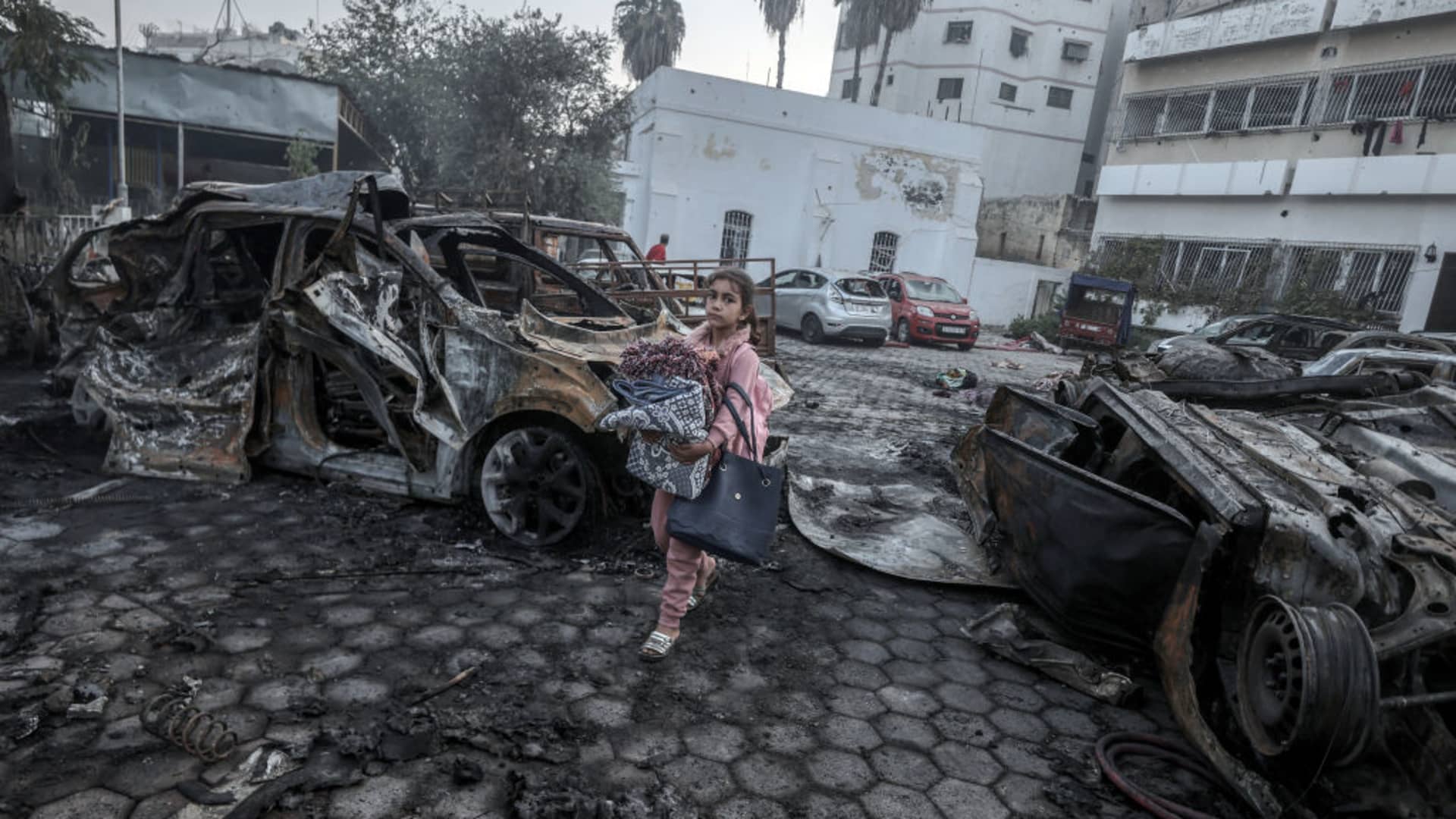 A girl tries to collect usable belongings amid wreckage of vehicles after Al-Ahli Baptist Hospital was hit in Gaza City, Gaza on October 18, 2023. 