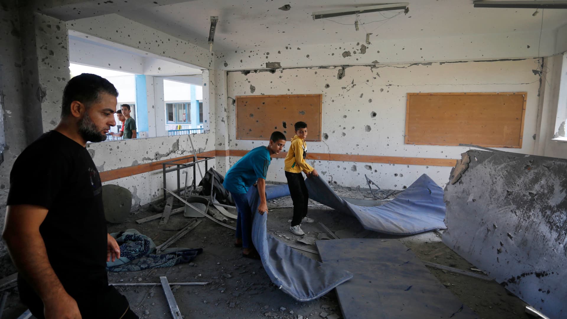 Young men remove mattresses in a shrapnel-pocked room inside a UN-run school in the refugee camp of Al-Maghazi in the central Gaza Strip, a day after at least 6 people were killed in a reported Israeli strike, on October 18, 2023. 