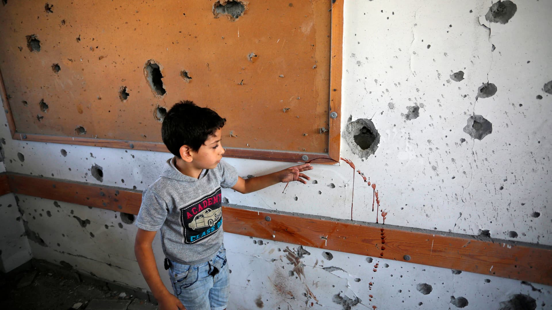 A young boy points at a blood stain across a shrapnel-pocked wall inside a UN-run school in the refugee camp of Al-Maghazi in the central Gaza Strip, a day after at least 6 people were killed in a reported Israeli strike, on October 18, 2023.