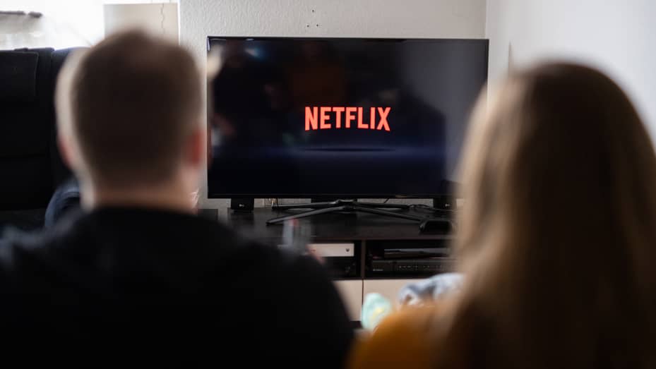 Um casal está sentado em frente a uma televisão com o logotipo da Netflix.