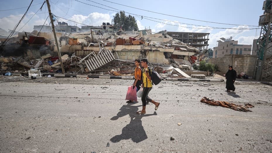 Residents walk through the road as the rubble of residential buildings after Israeli airstrikes at al-Zahra neighborhood in Gaza Strip on October 19, 2023.