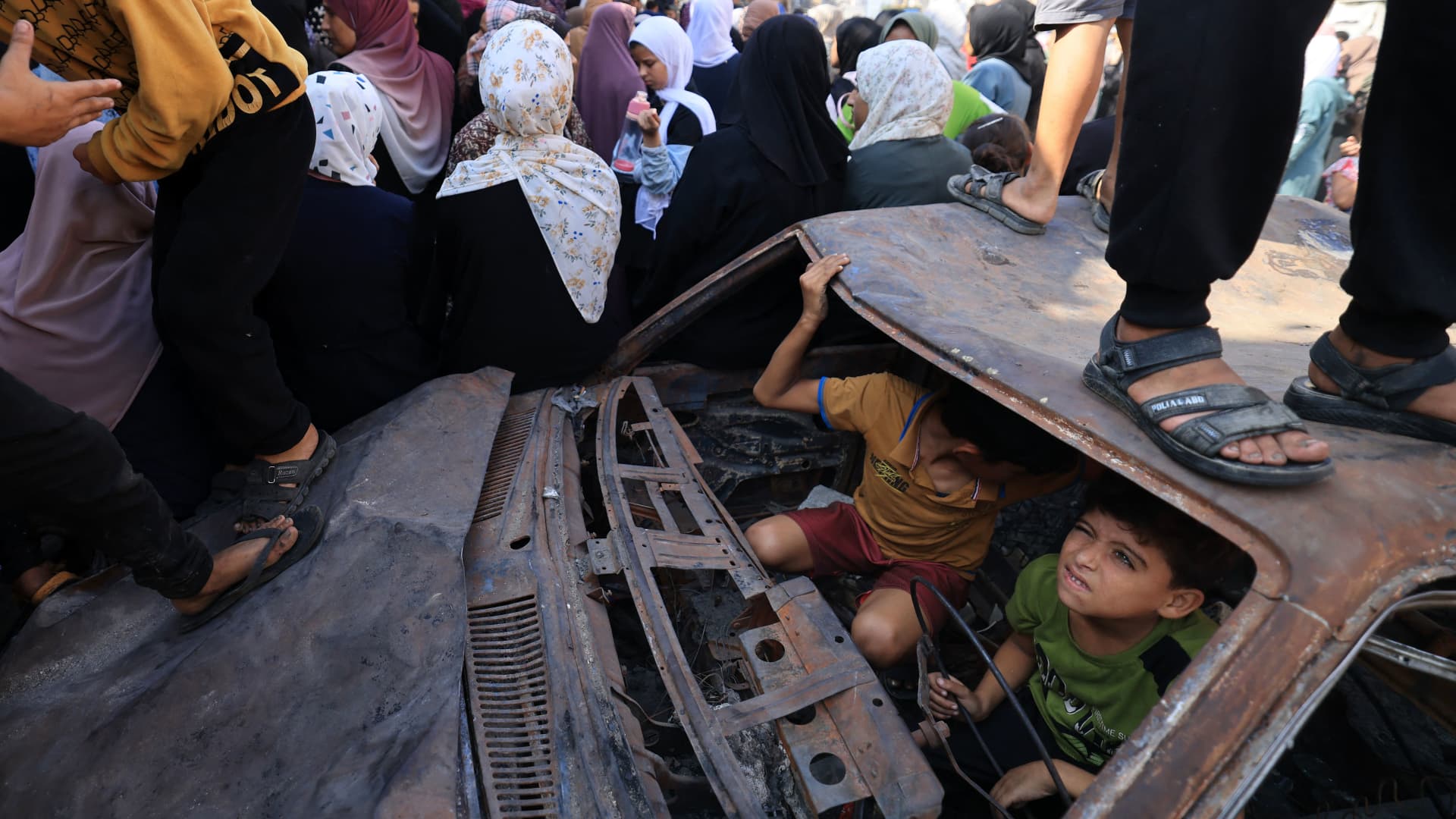 Children play in a charred car as people queue for bread in front of a bakery that was partially destroyed in an Israeli strike, in the Nuseirat refugee camp in the central Gaza Strip, on November 2, 2023, as battles continue between Israel and the Palestinian Hamas movement.