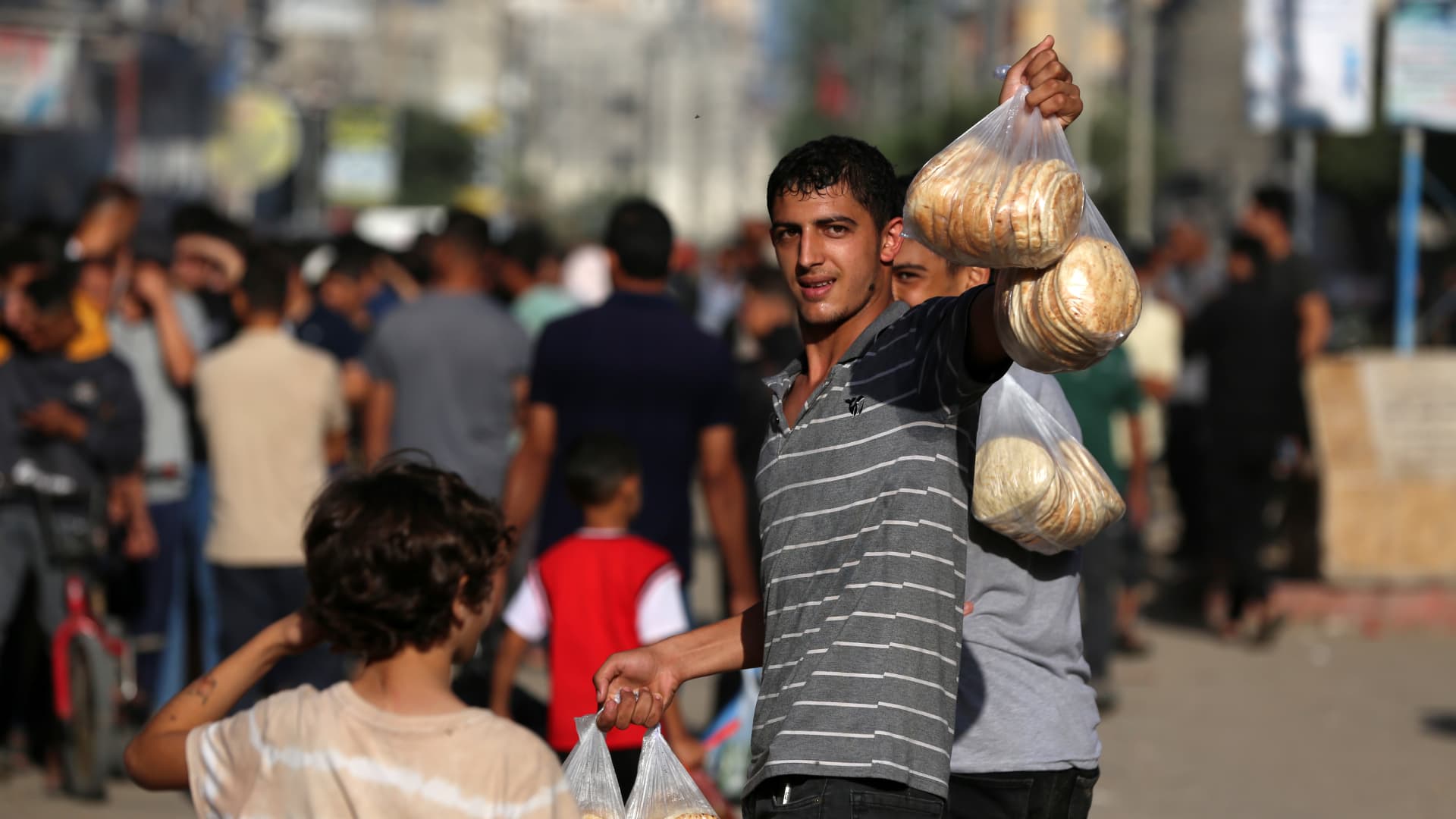 People carry bags of bread as others queue in front of a bakery that was partially destroyed in an Israeli strike, in the Nuseirat refugee camp in the central Gaza Strip, on November 4, 2023, as battles continue between Israel and the Palestinian Hamas movement. 