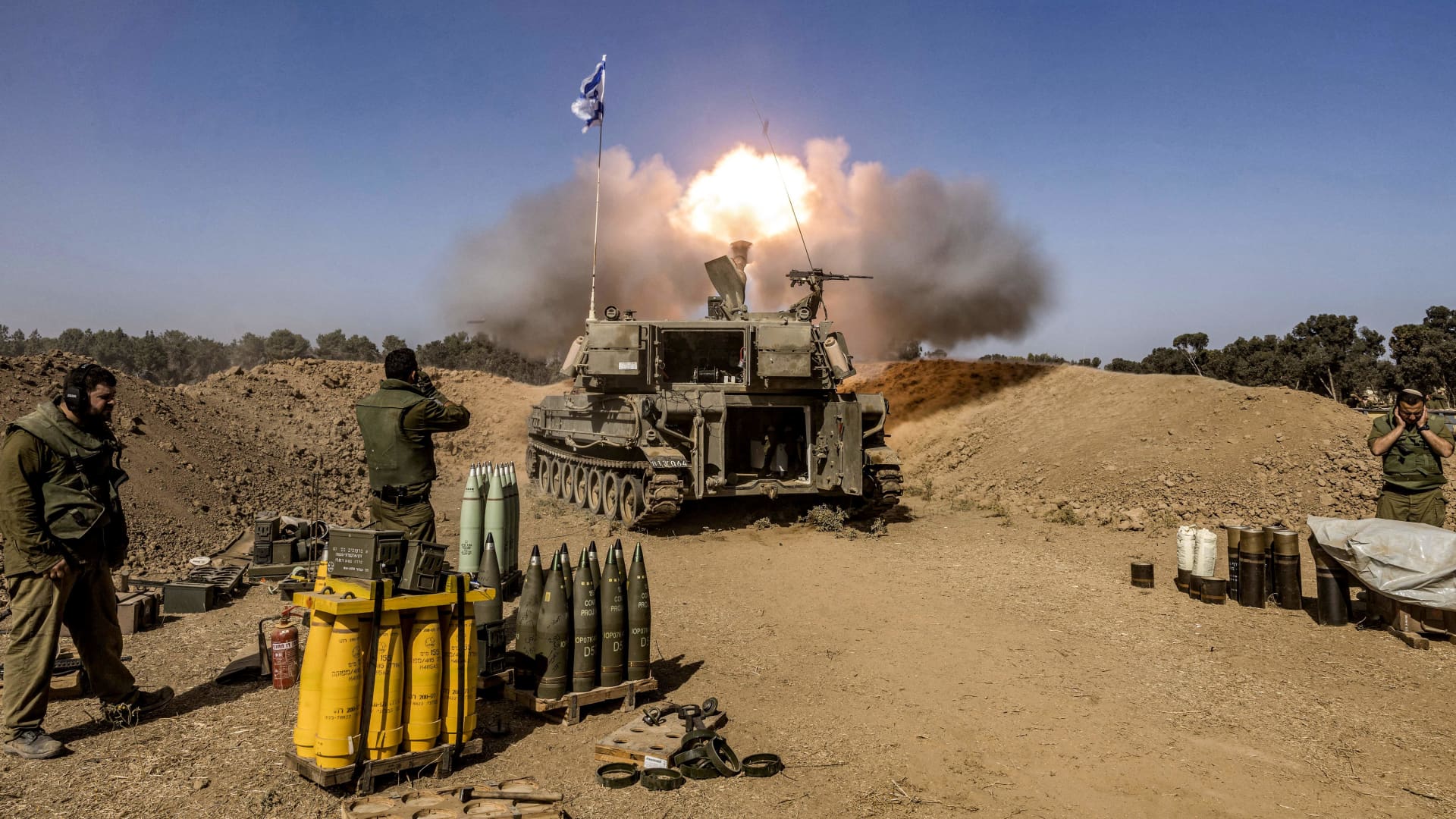 Israeli army soldiers cover their ears as a self-propelled artillery howitzer fires rounds from a position near the border with the Gaza Strip in southern Israel on November 6, 2023.