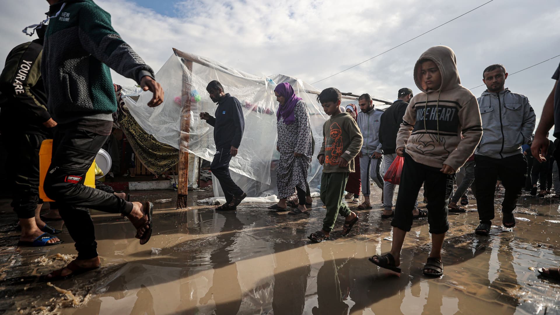 Children, adults are seen walking in water in the United Nations Relief and Works Agency (UNRWA) refugee camp located in Khan Younis, Gaza where displaced Palestinian families take shelter as Israeli attacks on Gaza continue on November 15, 2023. 