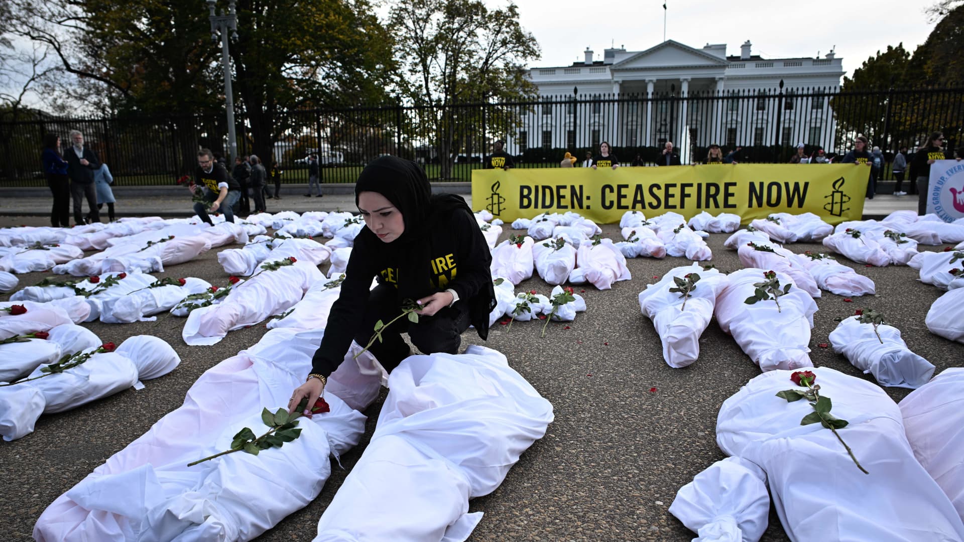 A demonstrator places flowers on white-shrouded body bags representing victims in the Israel-Hamas conflict, in front of the White House in Washington, DC, on November 15, 2023.