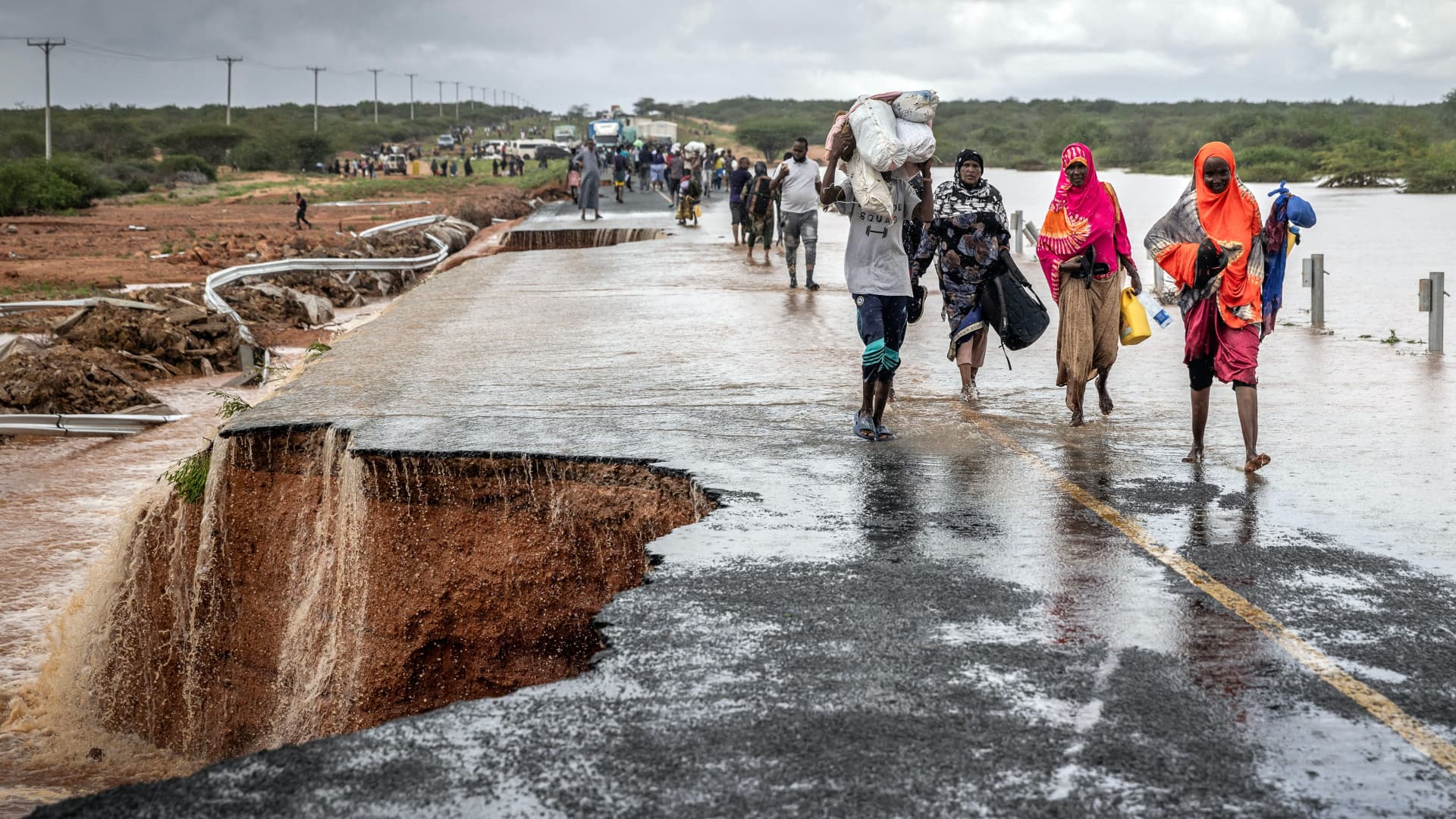 People carry their belongings while crossing the section of a road collapsing due to flash floods at the Mwingi-Garissa Road near Garissa on November 22, 2023. The Horn of Africa is experiencing torrential rainfall and floods linked to El Nino climate pattern. Several communities are isolated as thousands of homes have been destroyed or damaged by floods that struck at least 33 of Kenya's 47 counties, killing more than 70 people and displacing many across the East African nation. (Photo by LUIS TATO / AFP) (Photo by LUIS TATO/AFP via Getty Images)